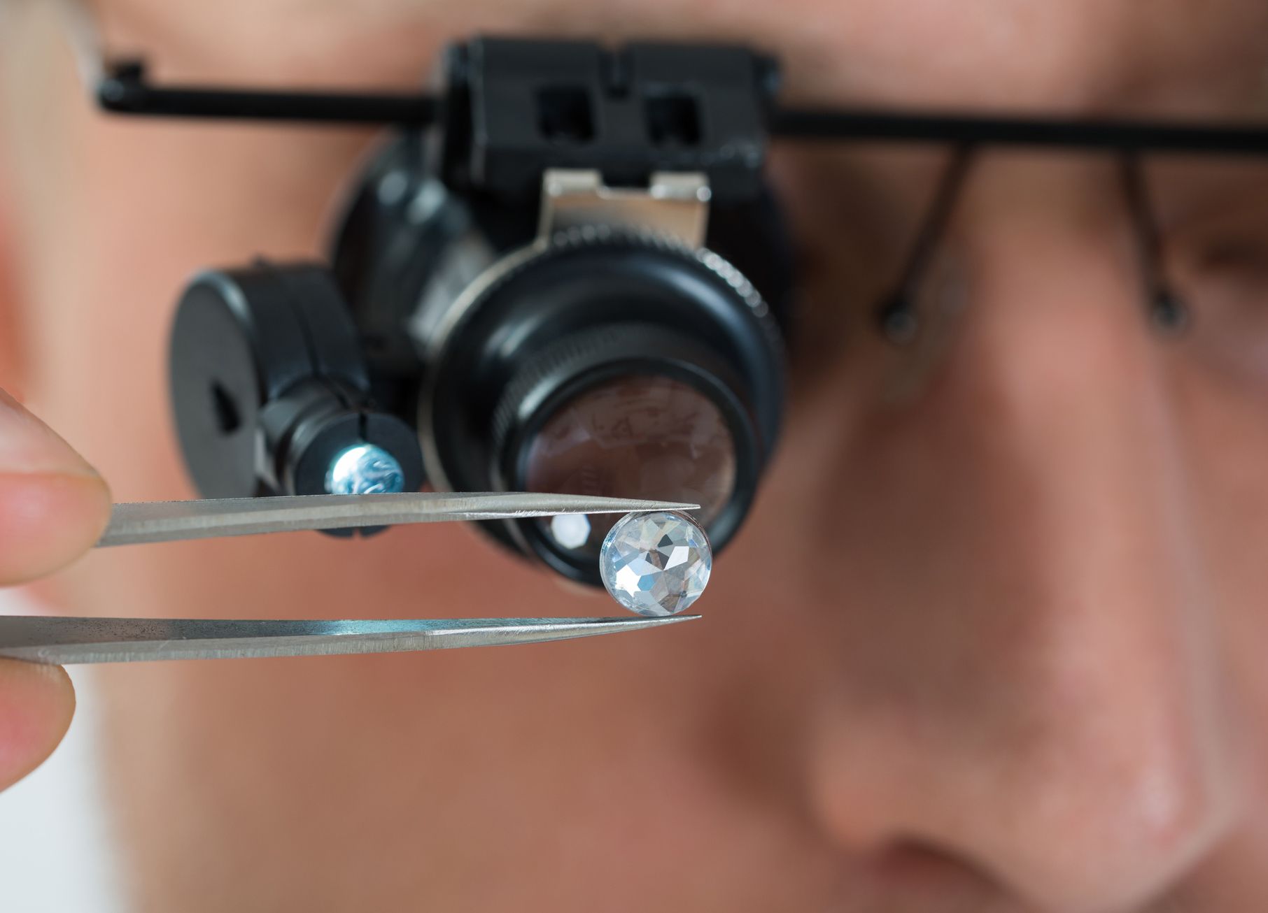 Person with magnifying glasses inspecting a diamond held by tweezers.