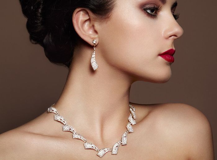 Woman wearing diamond necklace and earrings, red lipstick, brown background.