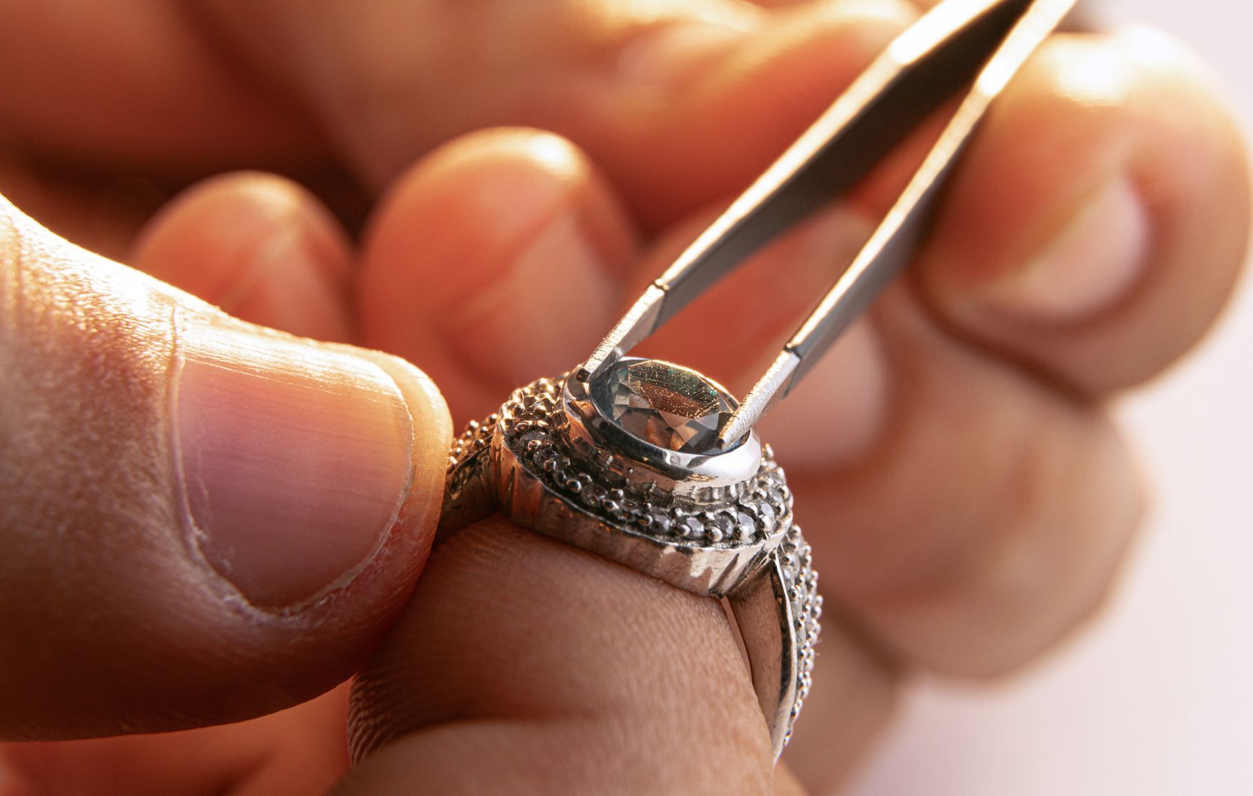 Jeweler's hands holding a diamond ring with tweezers, setting a stone.