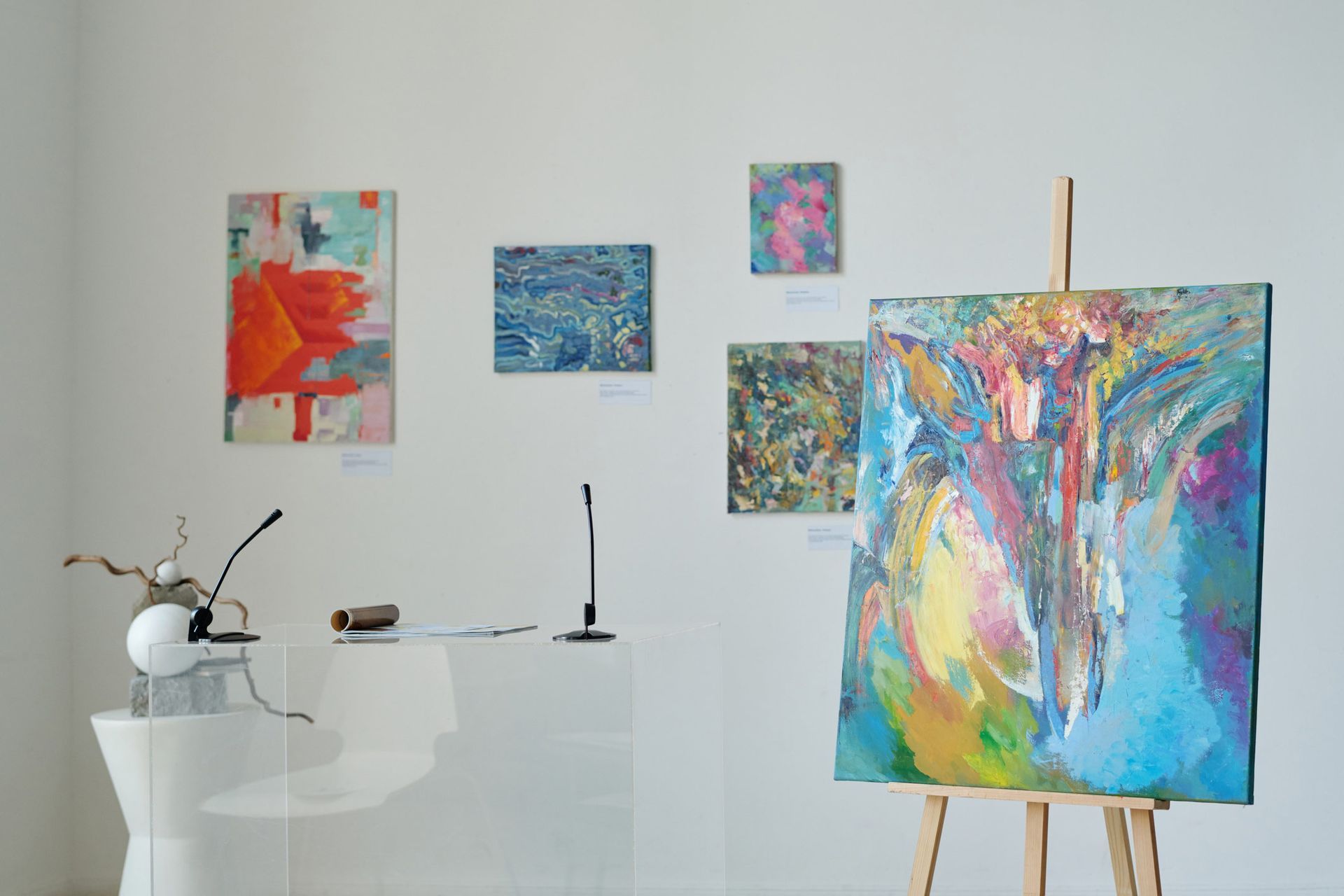 Art gallery with colorful abstract paintings on white walls; painting on an easel in the foreground.