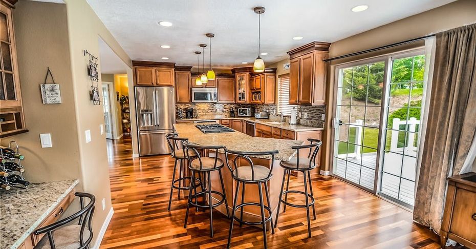 A kitchen with hardwood floors , stainless steel appliances , a large island and stools.