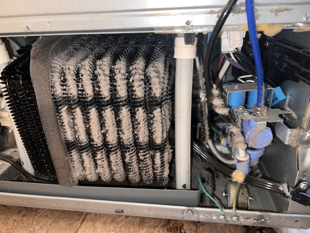 The inside of a refrigerator with a lot of wires coming out of it.