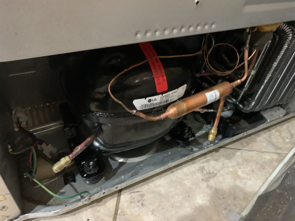 The inside of a refrigerator with a compressor and copper pipes.