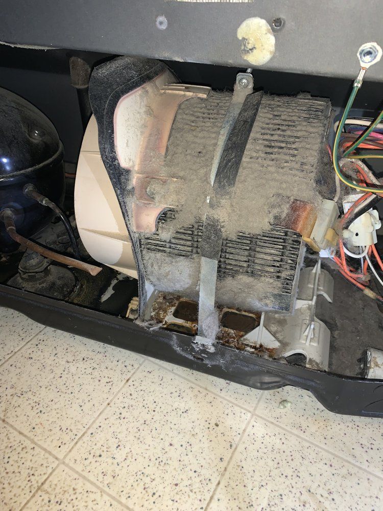 The inside of a refrigerator with a dirty motor sitting on the floor.