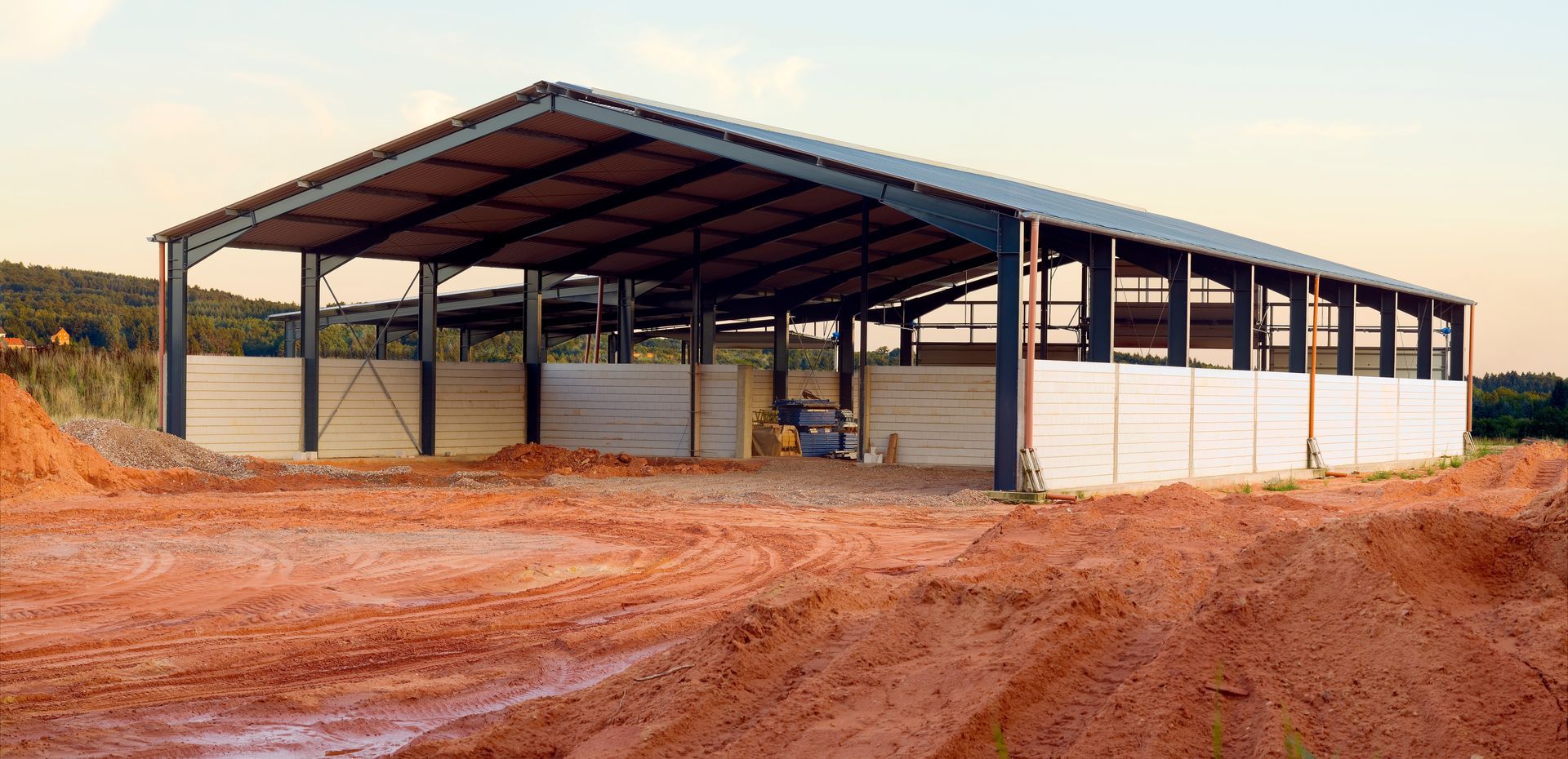 A partially constructed pole barn in a rural area with a clear sky in the background, built by skill