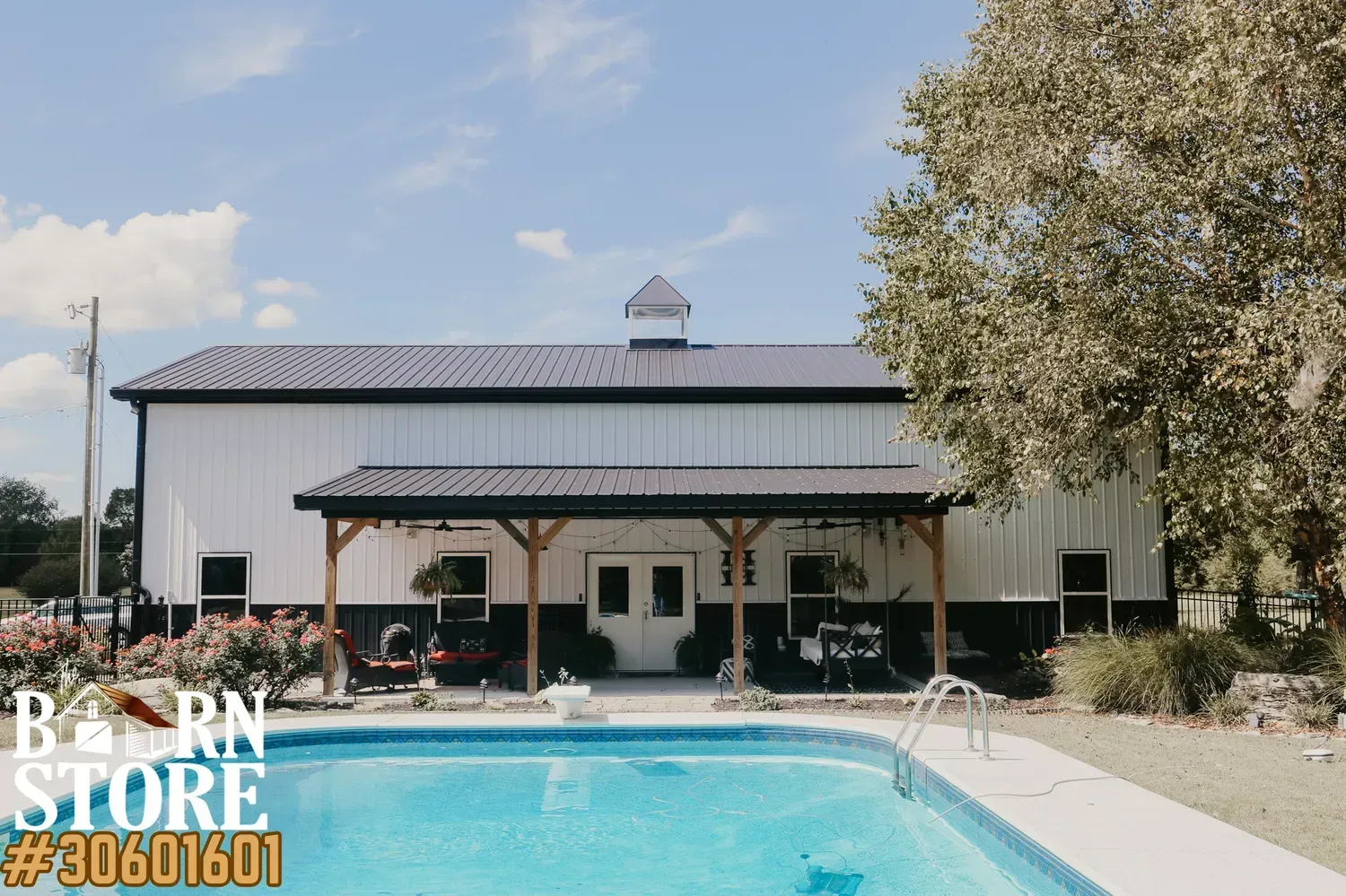 A large modern barn house with a white and black exterior, featuring an outdoor patio area and pool.