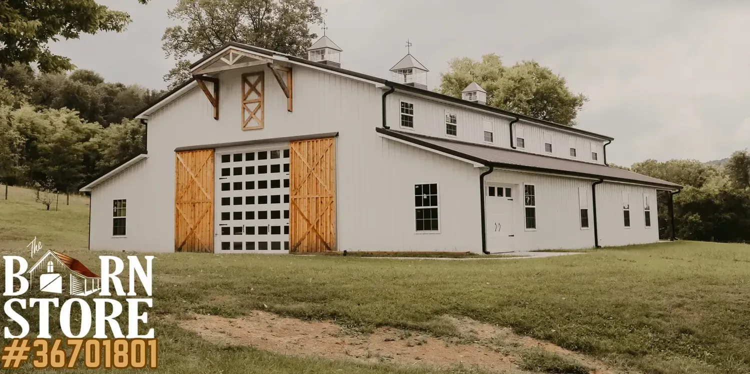 Large white barn house with wooden sliding doors and cupolas on the roof by barn builders near you.