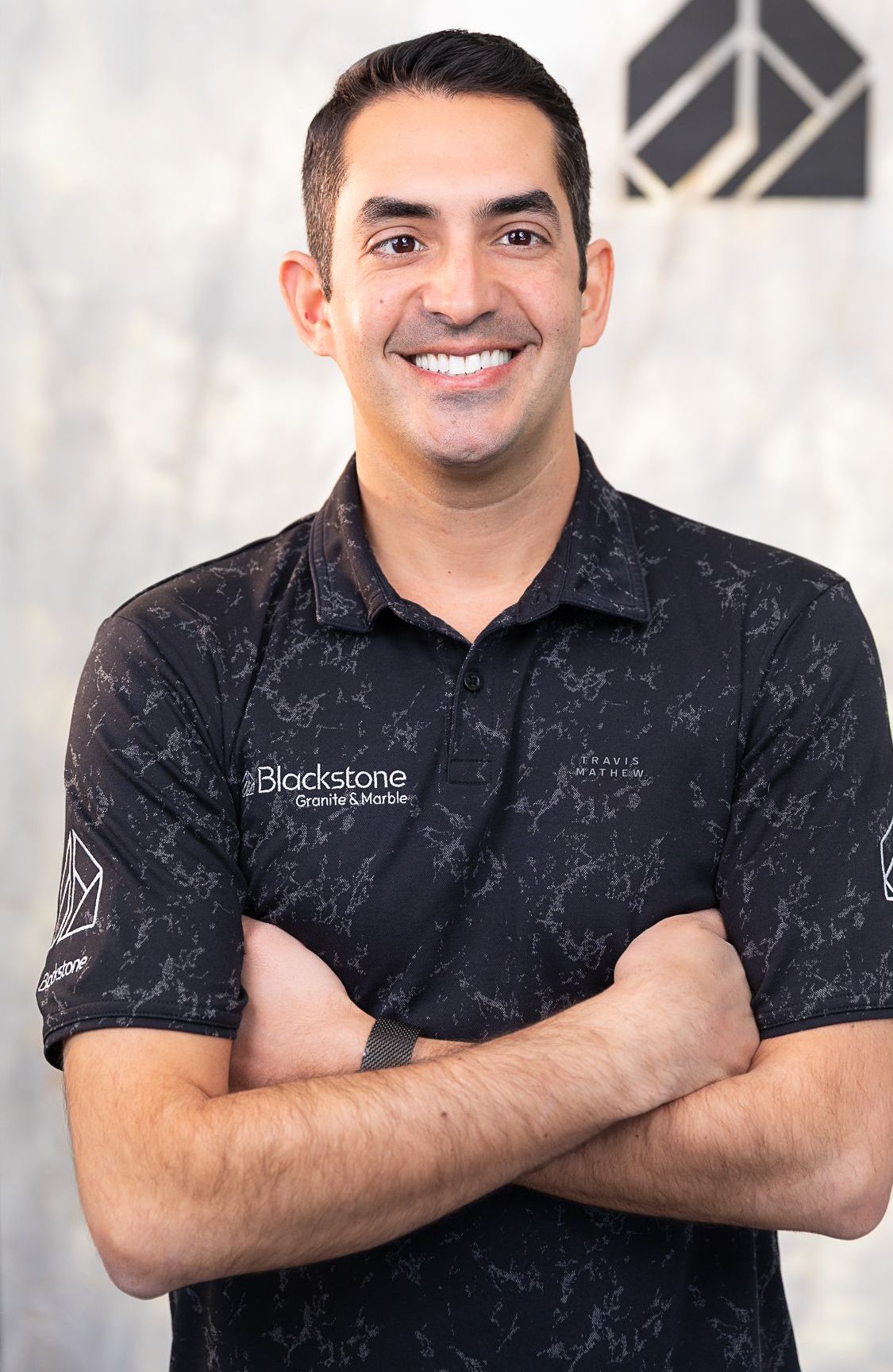 A man in a black shirt is smiling with his arms crossed.