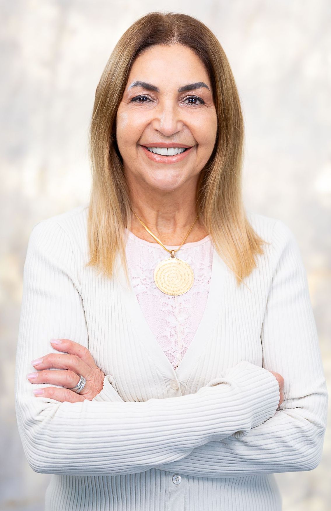 A woman in a white sweater is smiling with her arms crossed.