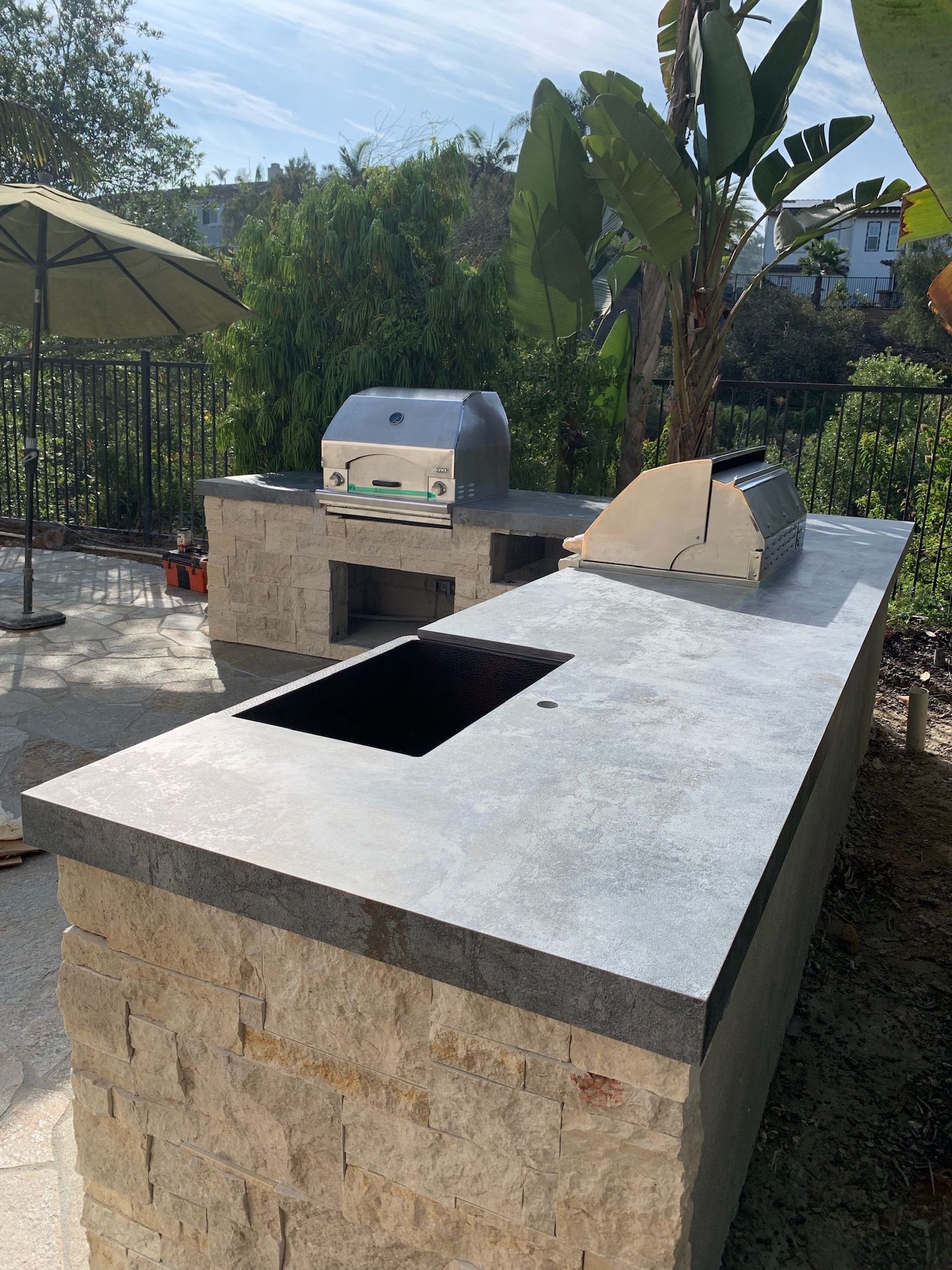 An outdoor kitchen with a grill, stone counter top, sink, and umbrella in San Diego.