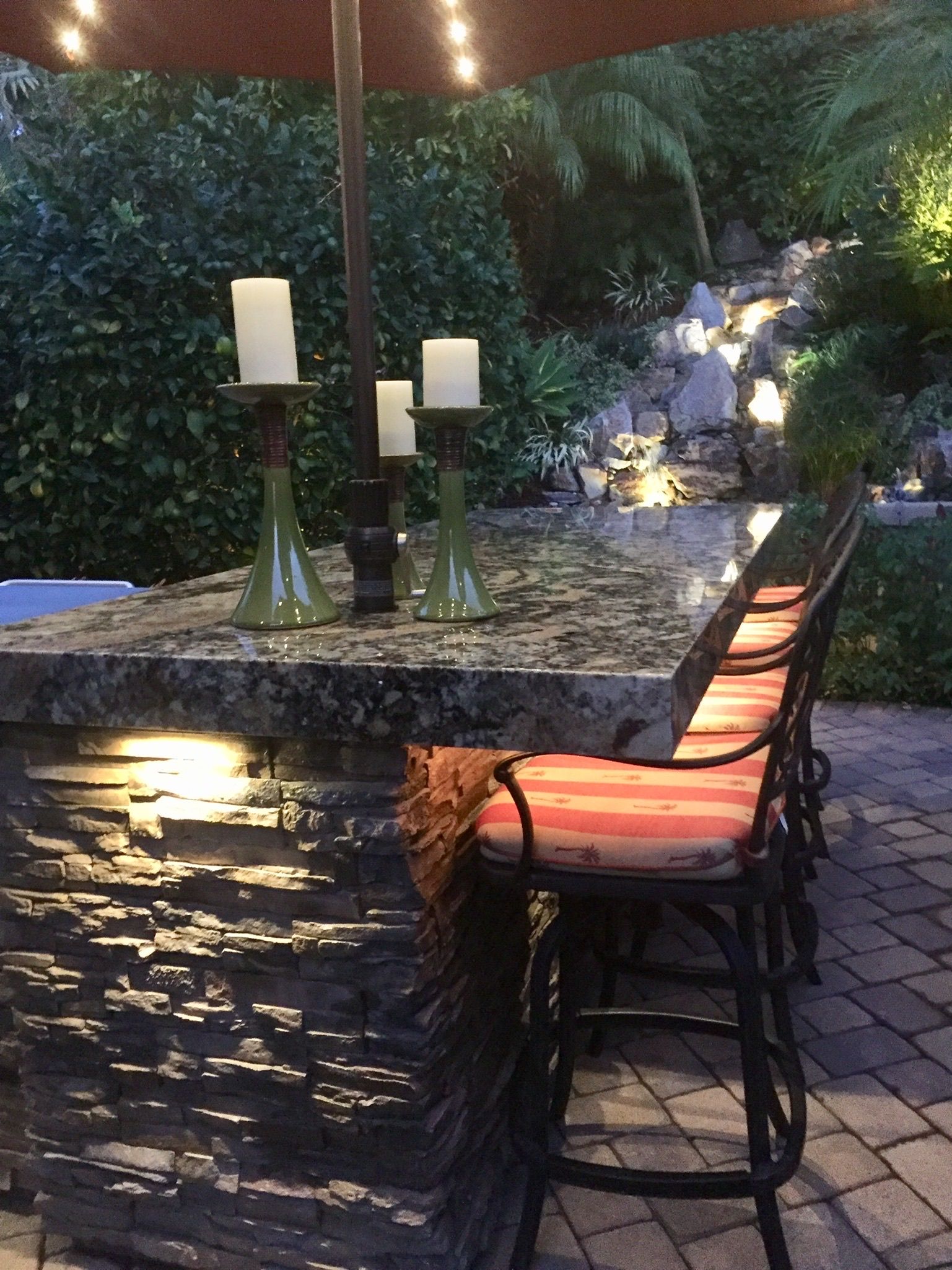 A bar made of dark granite with candles and a waterfall in the background