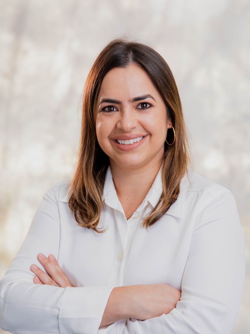 A woman in a white shirt is smiling with her arms crossed.
