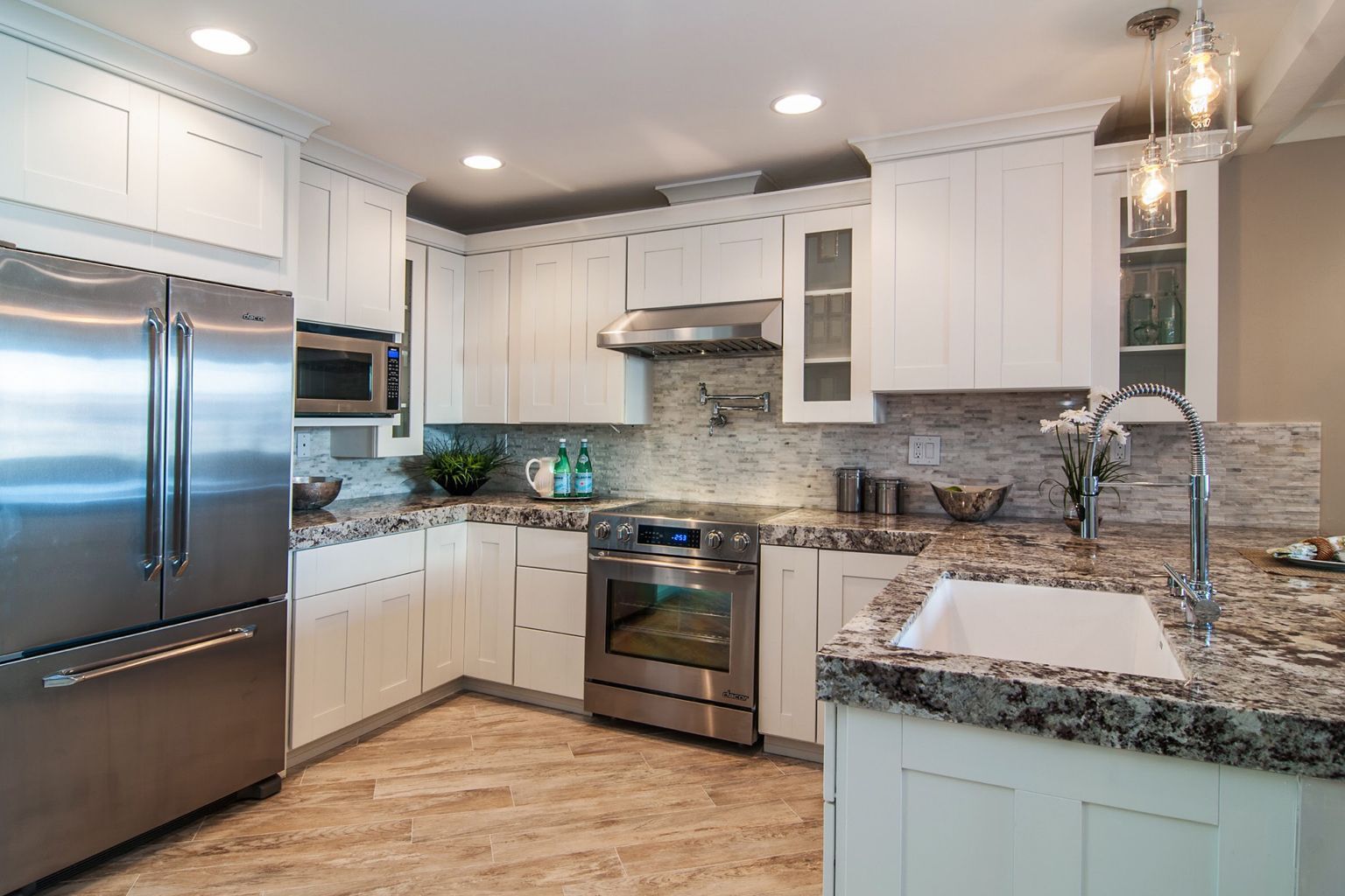 A kitchen with white cabinets , stainless steel appliances , granite counter tops and a sink.