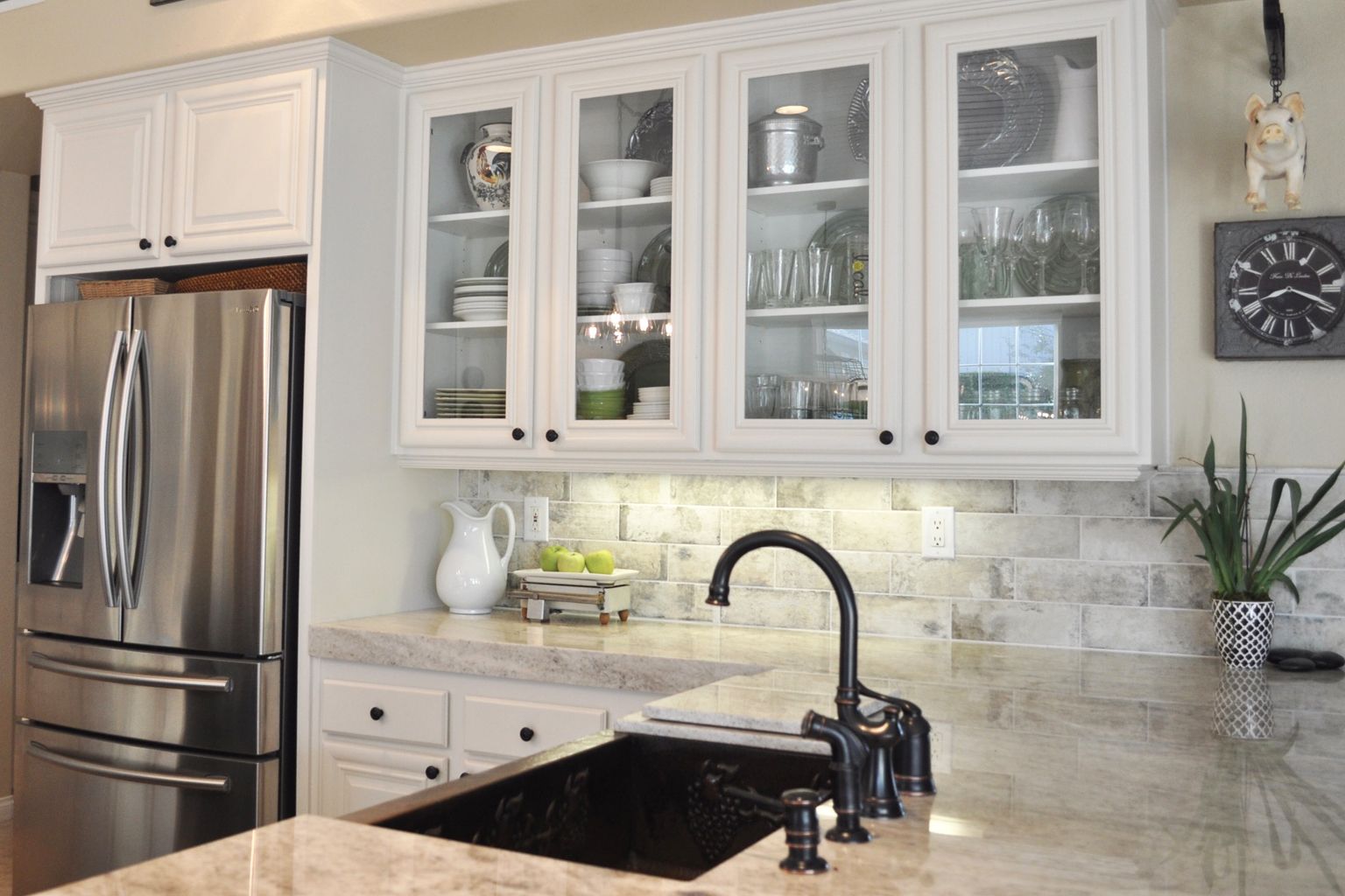 A kitchen with white cabinets , stainless steel appliances , a sink and a refrigerator.