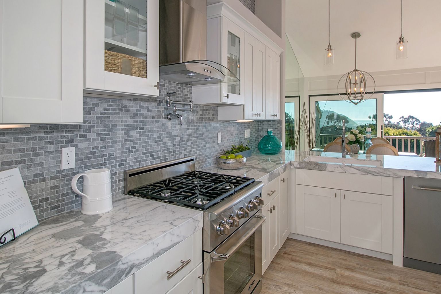 A kitchen with white cabinets , a stove , a dishwasher , and a window in San Diego.
