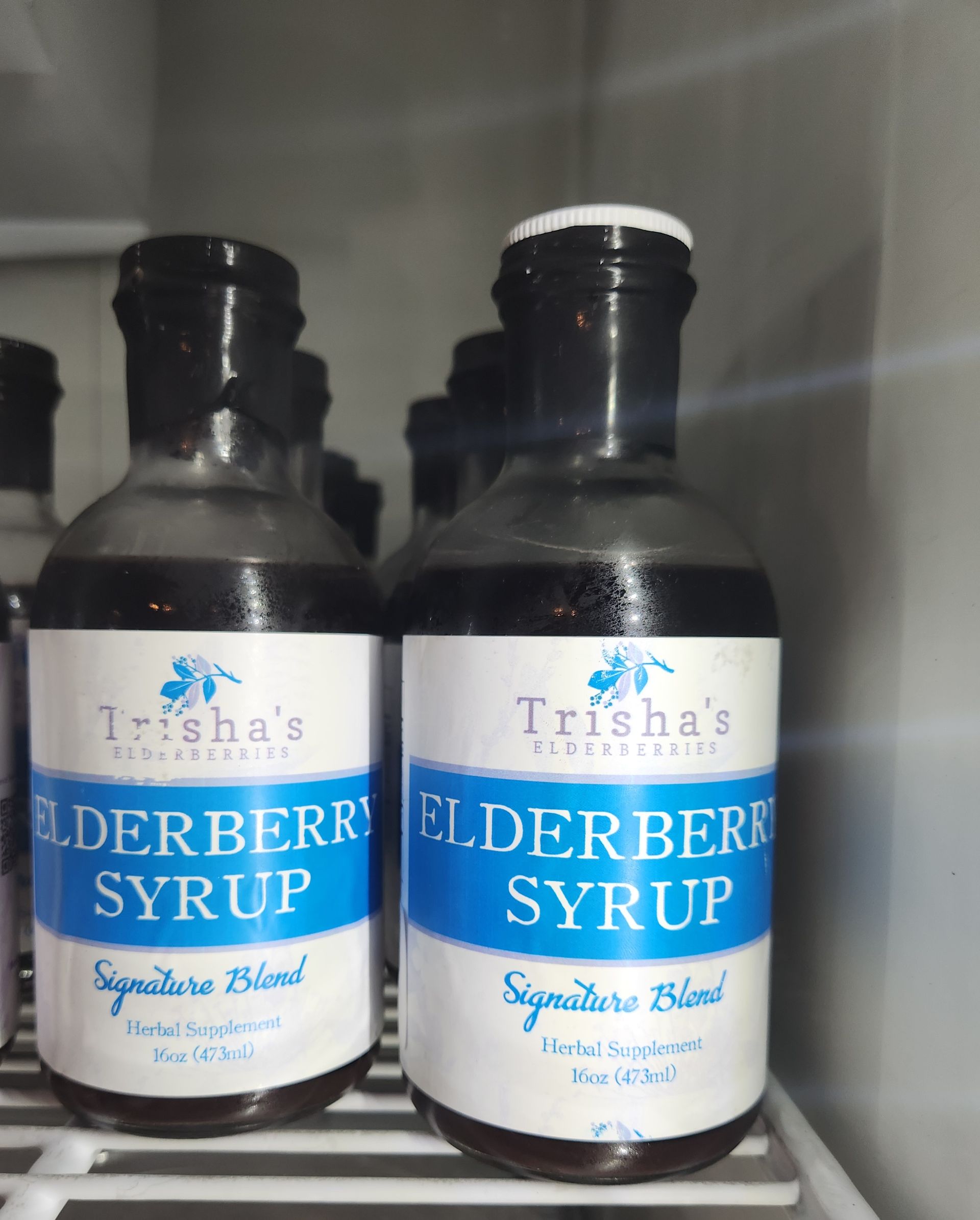 Two bottles of trisha 's elderberry syrup sit on a shelf