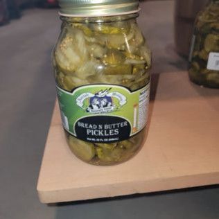 A jar of pickles is sitting on a wooden cutting board.