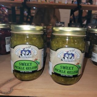 Two jars of sweet pickle relish are sitting on a wooden table.