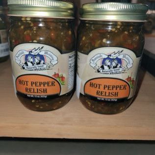Two jars of hot pepper relish are sitting on a wooden table.