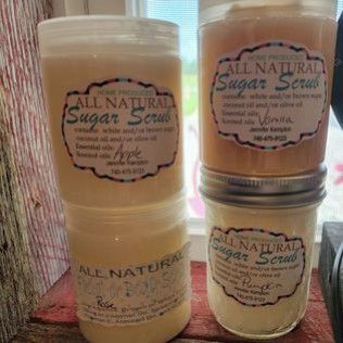 Three jars of all natural sugar scrub are stacked on top of each other on a wooden table.