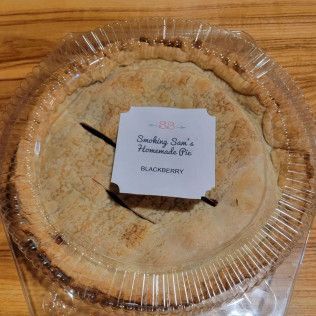 A blackberry pie is in a plastic container on a wooden table.