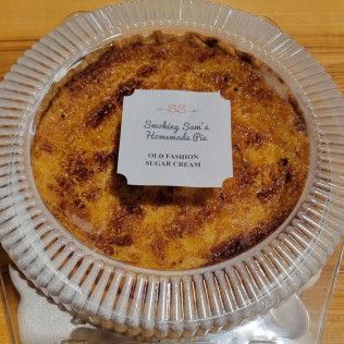 A pie is in a plastic container on a wooden table.