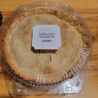 A cherry pie is in a plastic container on a wooden table.