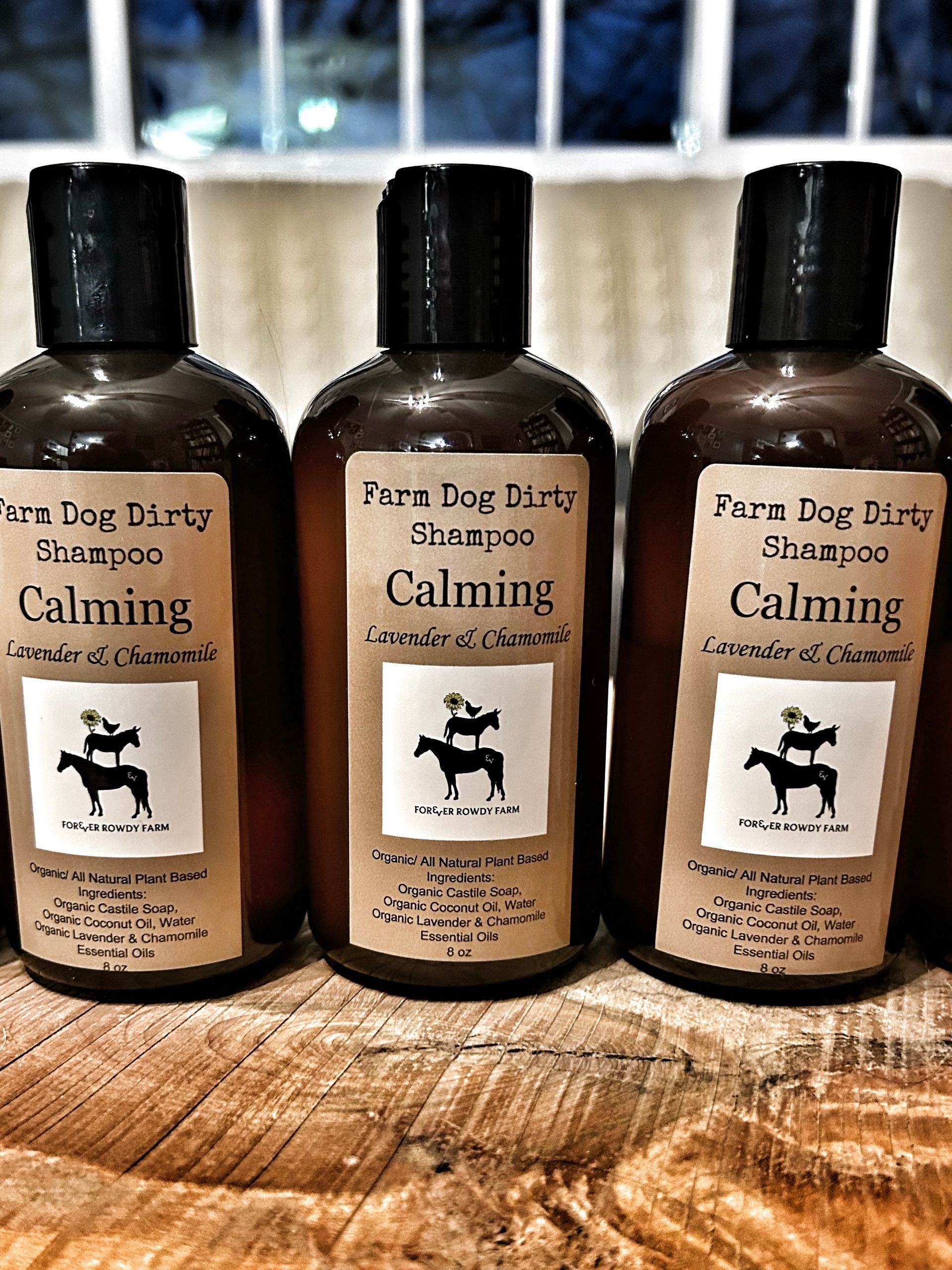 Three bottles of farm dog dirty shampoo are sitting on a wooden table