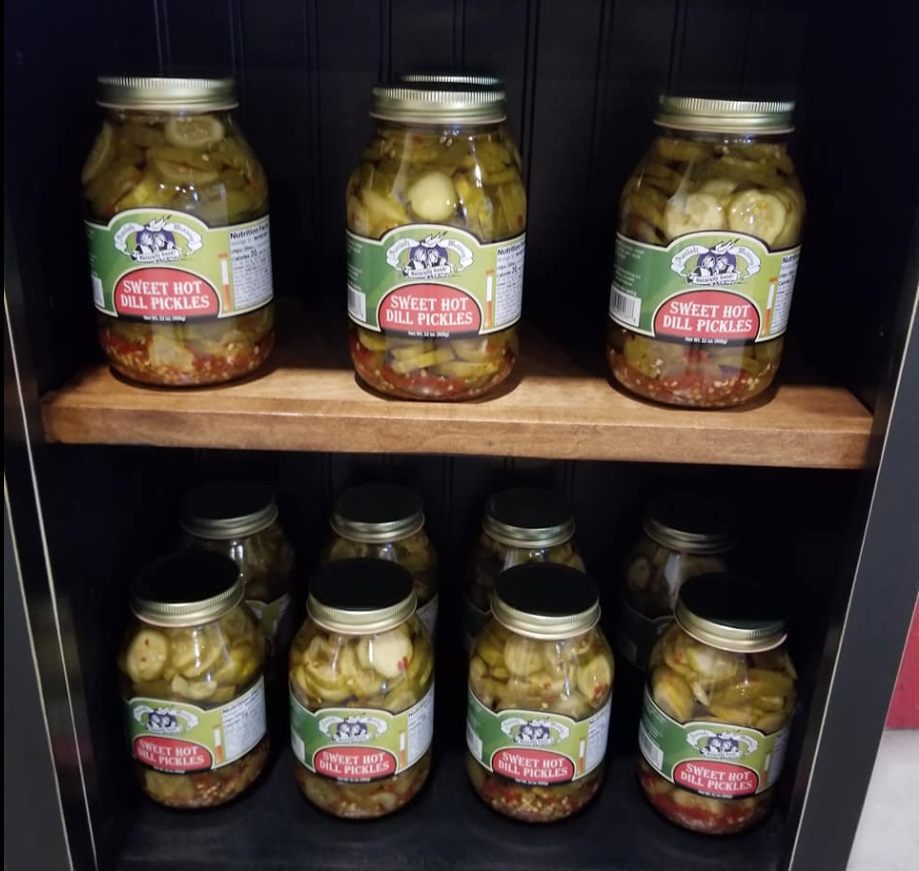 Several jars of pickles are on a wooden shelf