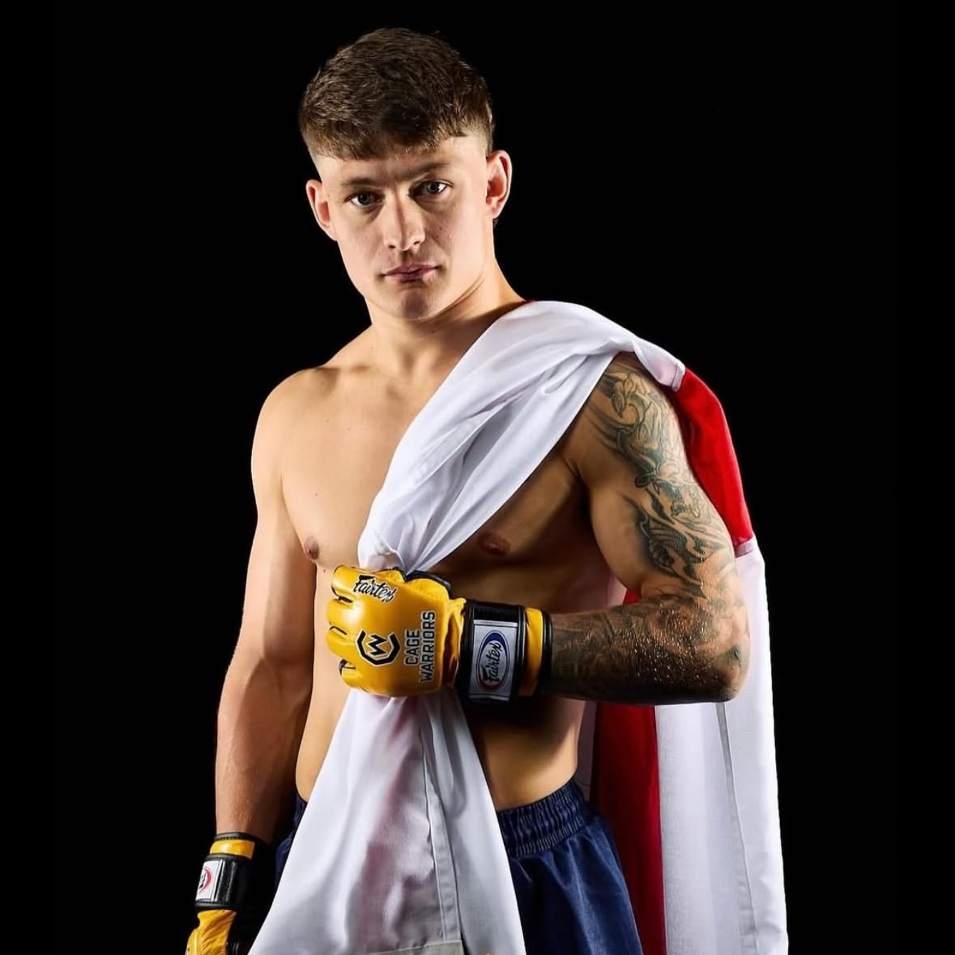 Man with arm tattoos draped in English flag, wearing MMA gloves.