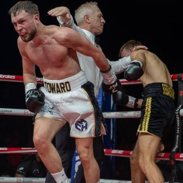 Boxer in white trunks throws a punch, referee in the middle, other boxer in black trunks.