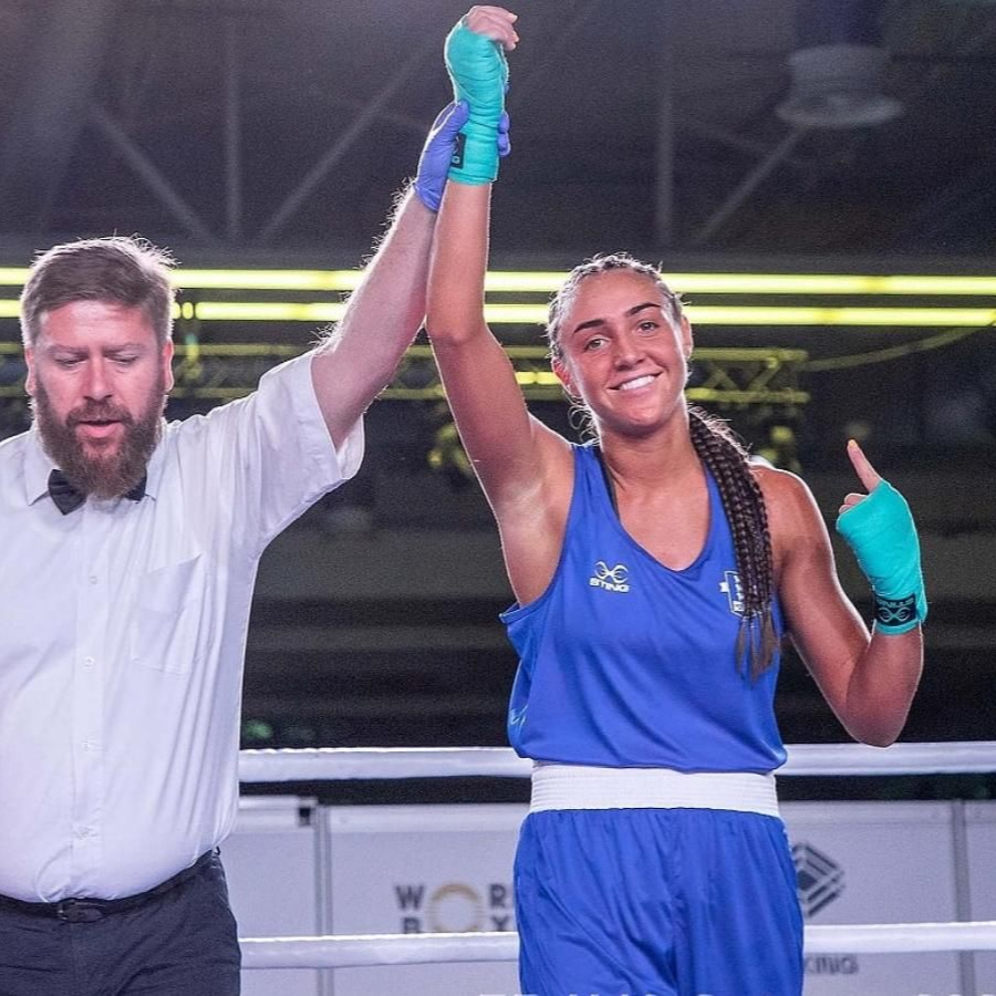 Boxer in blue uniform raises arm, victorious, with referee in ring.