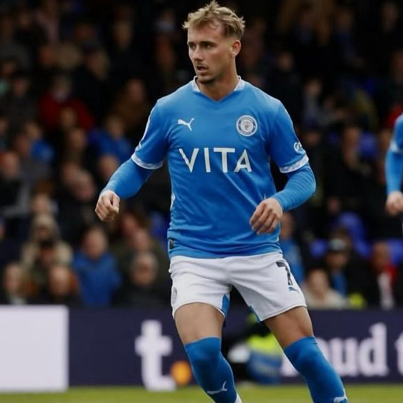 Soccer player in blue jersey and shorts on a field; a crowd in the background.