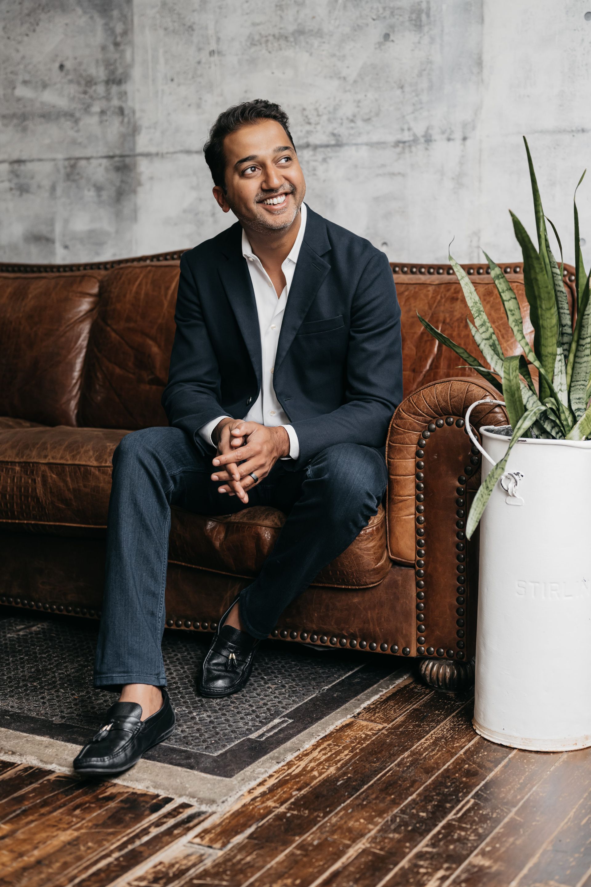 A corporate executive in a suit sitting on a couch with a potted plant.