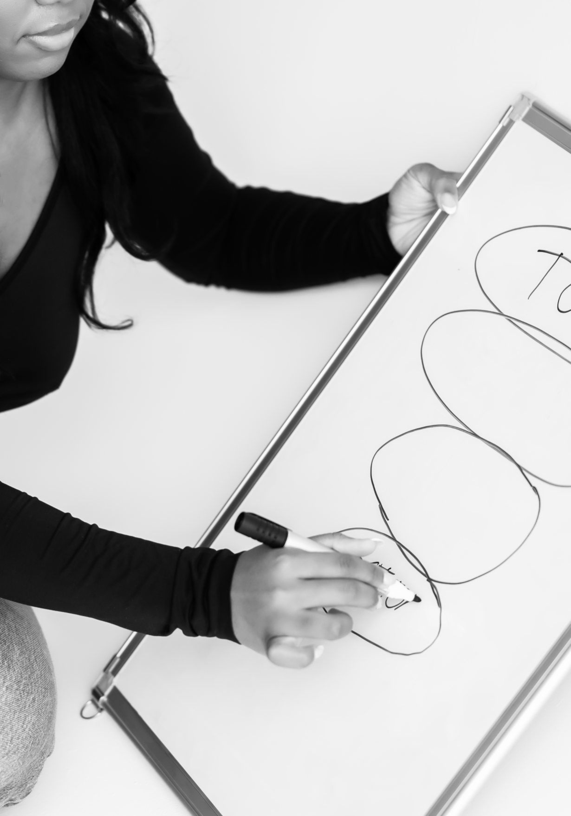 A black and white photo of a woman writing on a white board