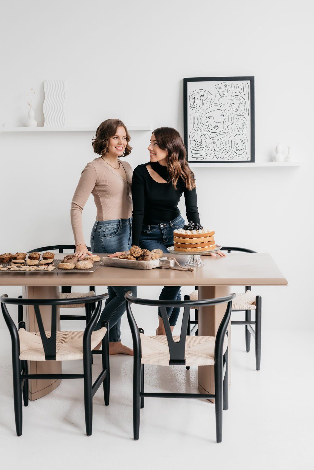 Two entrepreneurs standing close to each other with their freshly baked cooking, muffins, and cake organized on the dining room table