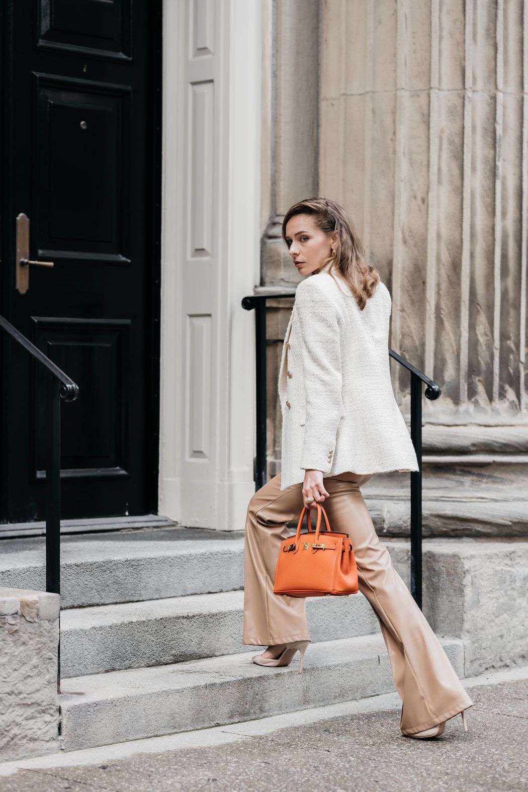 A woman is walking down a set of stairs holding an orange bag.