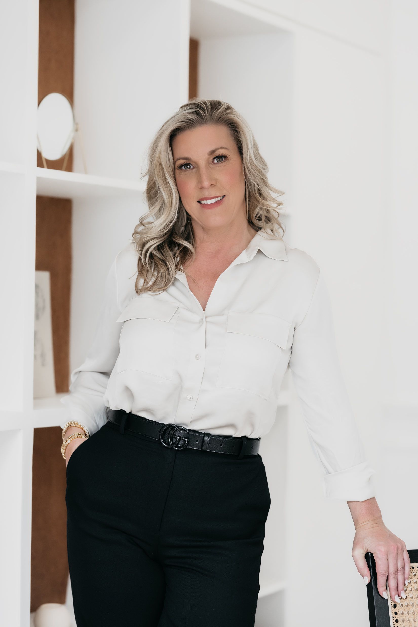 A woman in a white shirt and black pants is standing in front of a bookshelf.