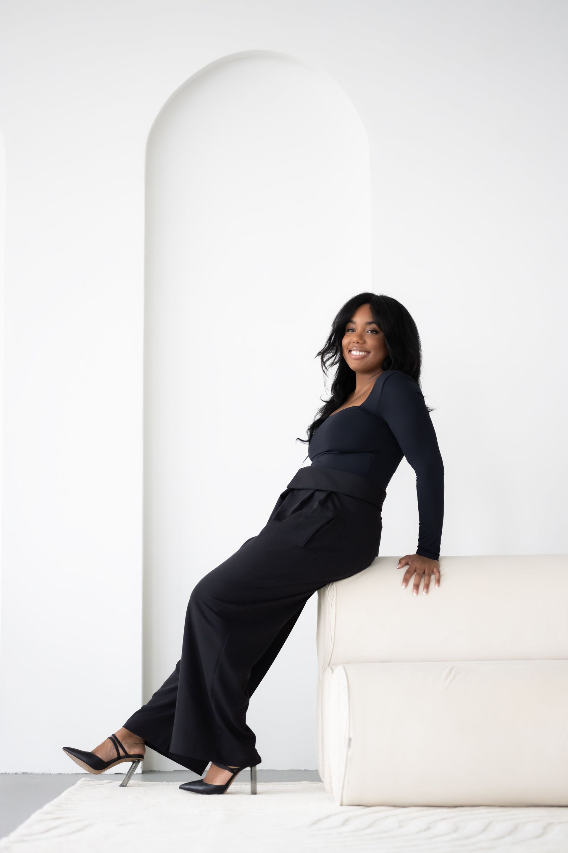 A marketing professional sits gracefully on the floor in an all-black ensemble, her contemplative expression highlighting a moment of creativity and strategy.