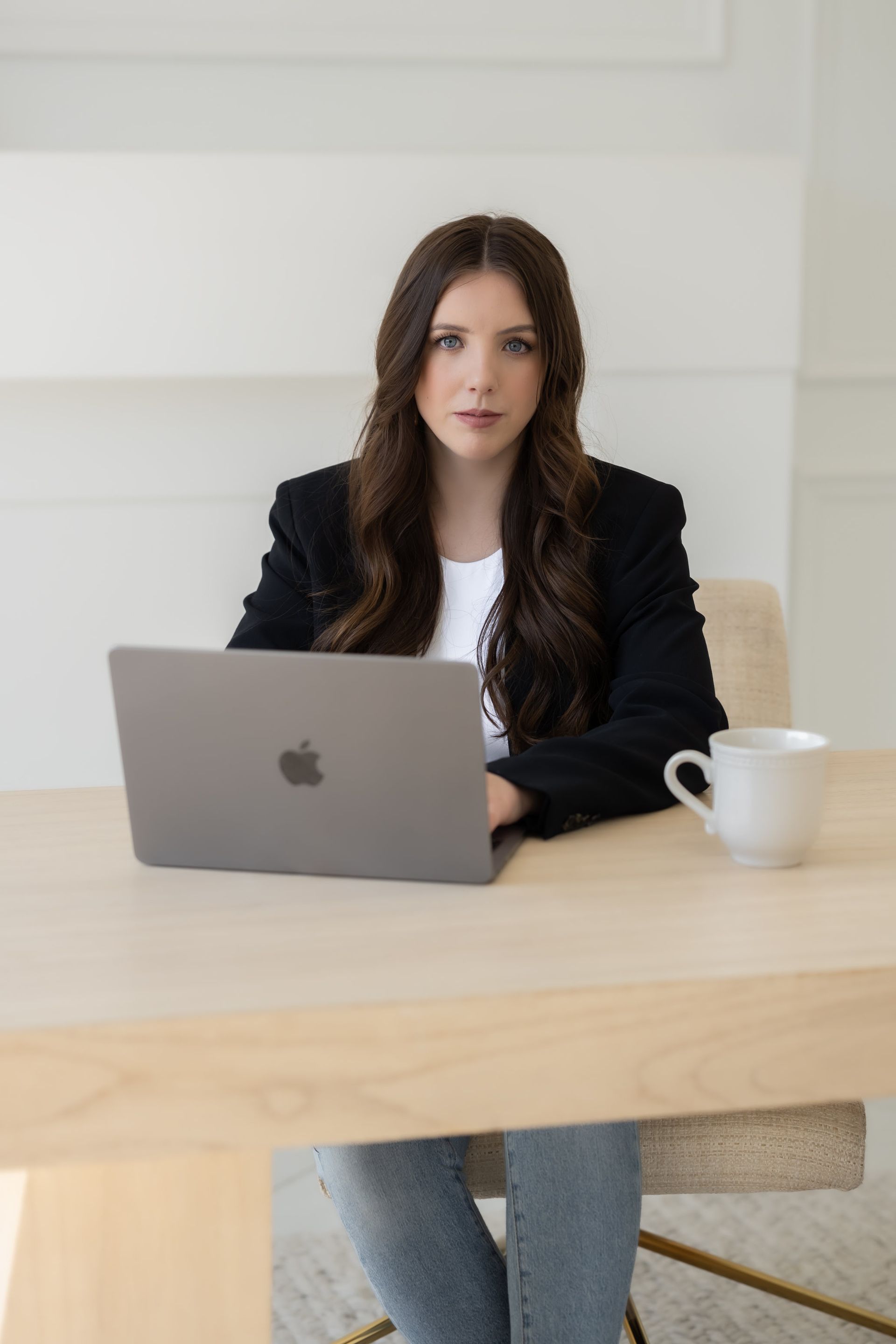 A woman is sitting at a table with a laptop and a cup of coffee.