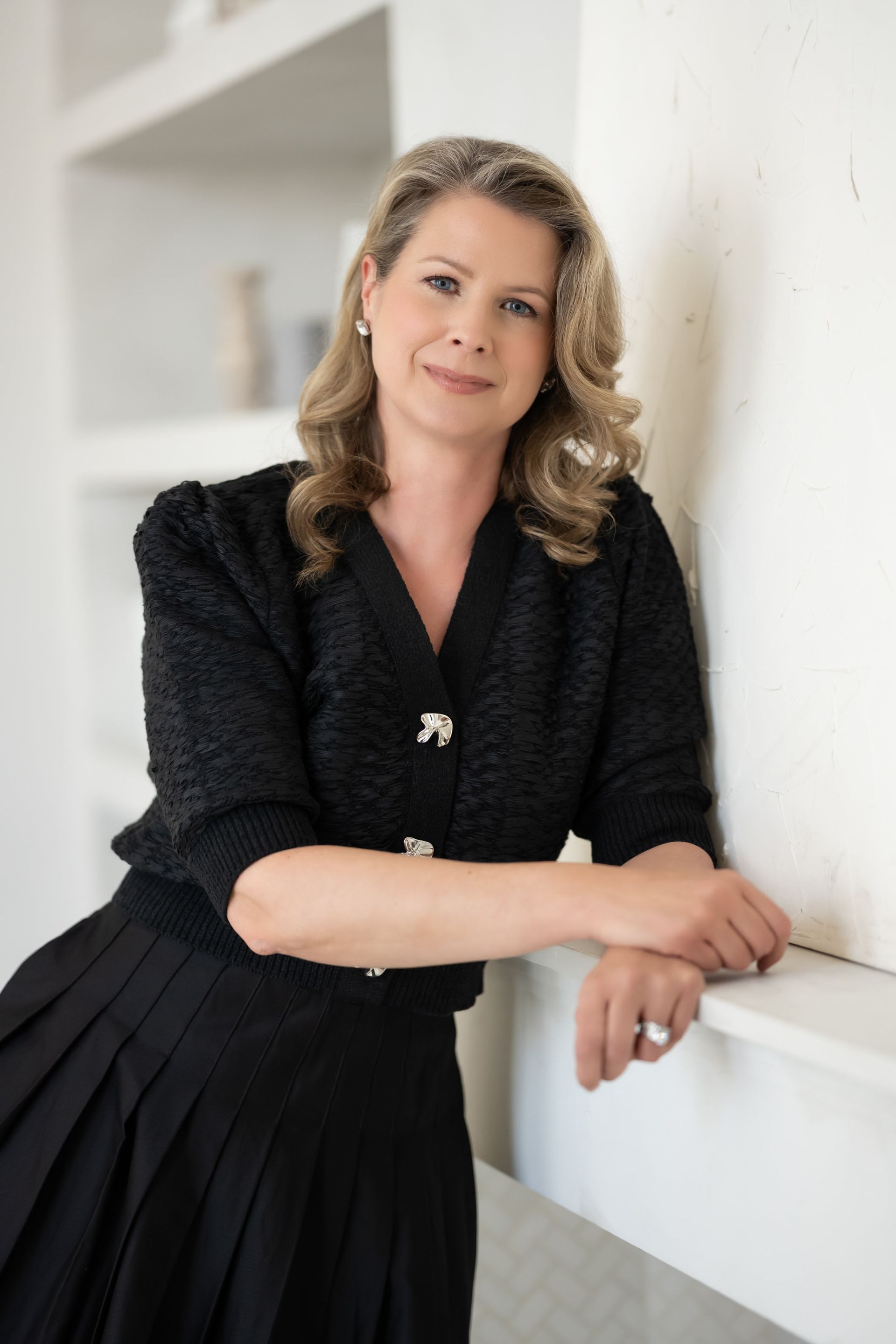 A woman in a black dress is leaning against a wall.