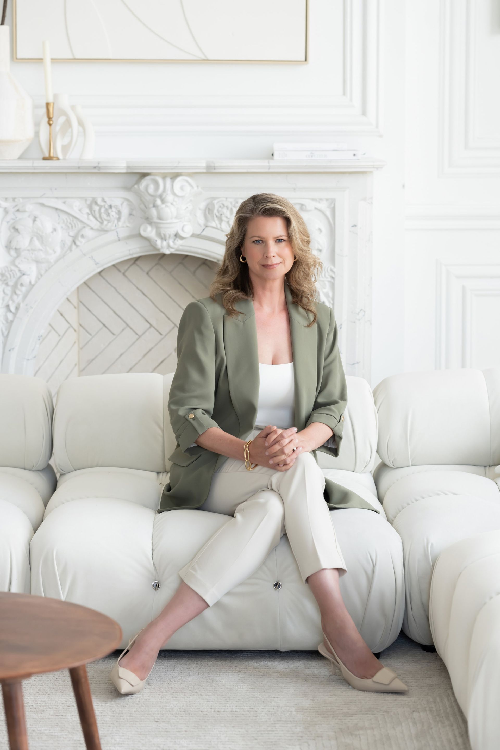 A woman is sitting on a white couch in front of a fireplace.