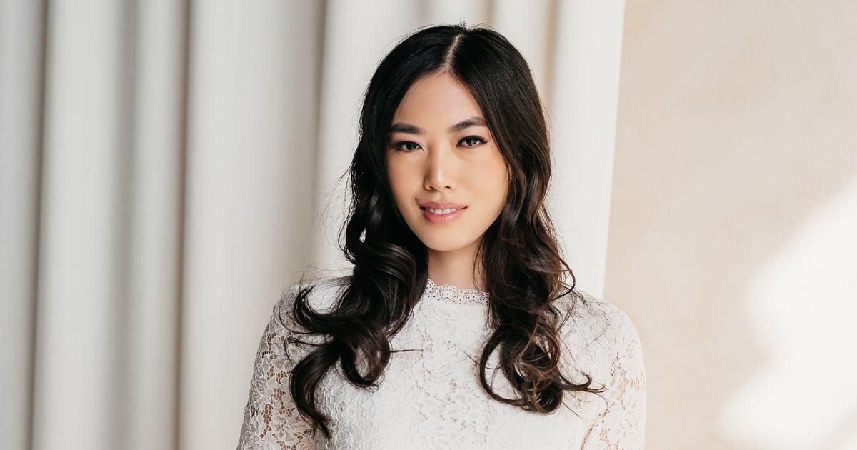 A woman in a white lace dress is standing in front of a white curtain.