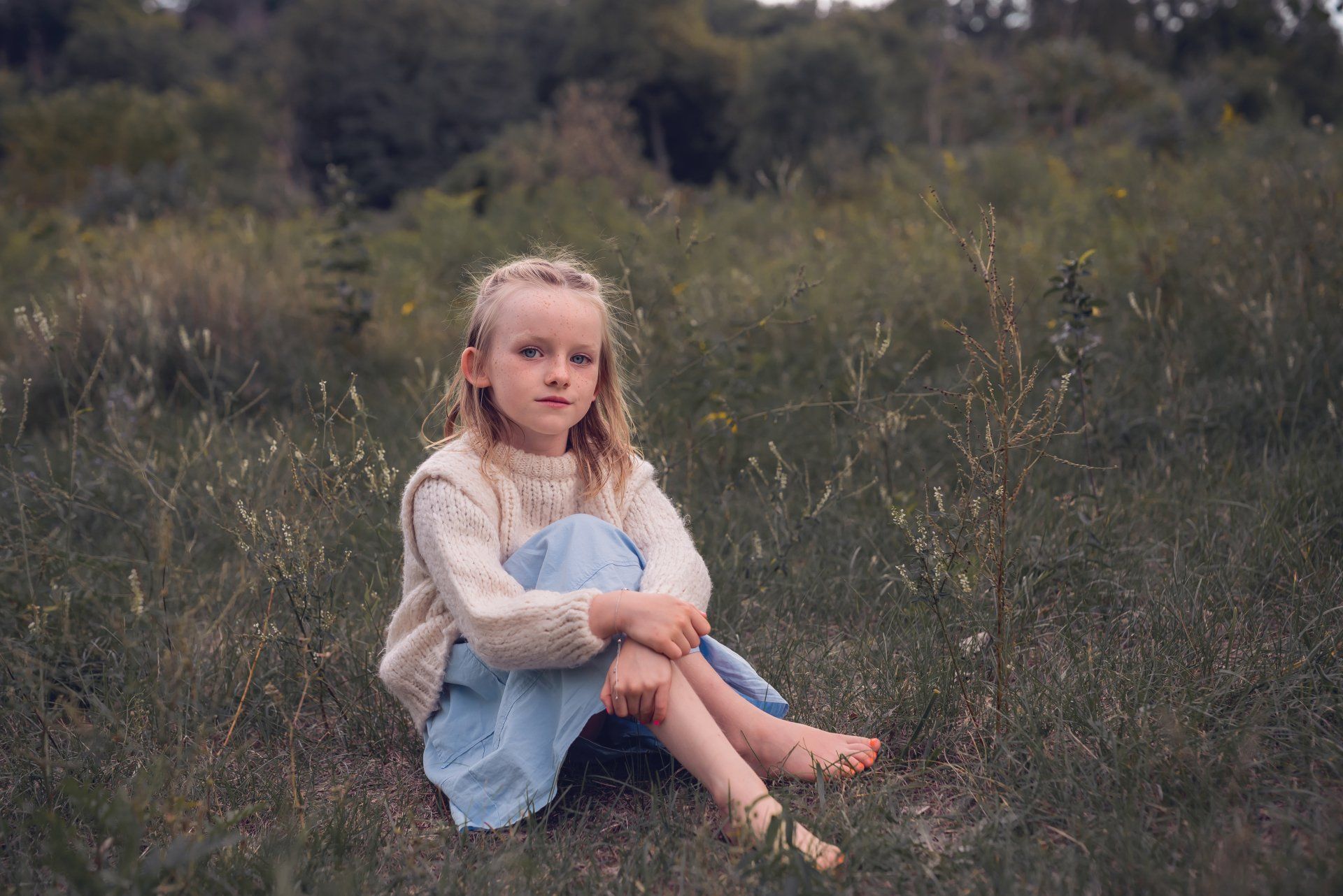 young girl with blonde hair sitting in a grassy field