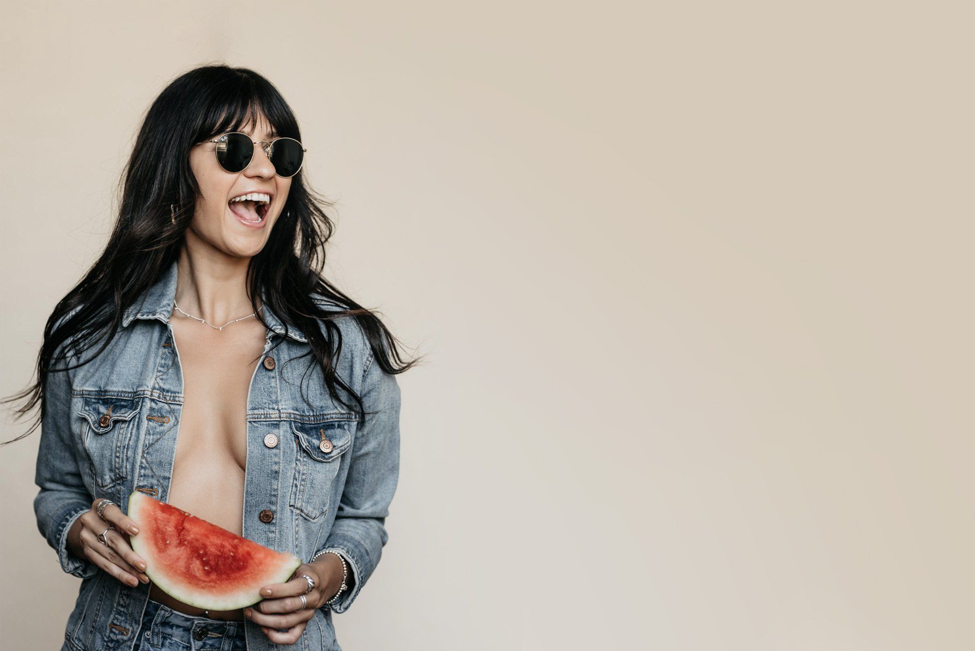 A beautiful young woman smiles while wearing dark sun glasses and holds a slice of watermelon
