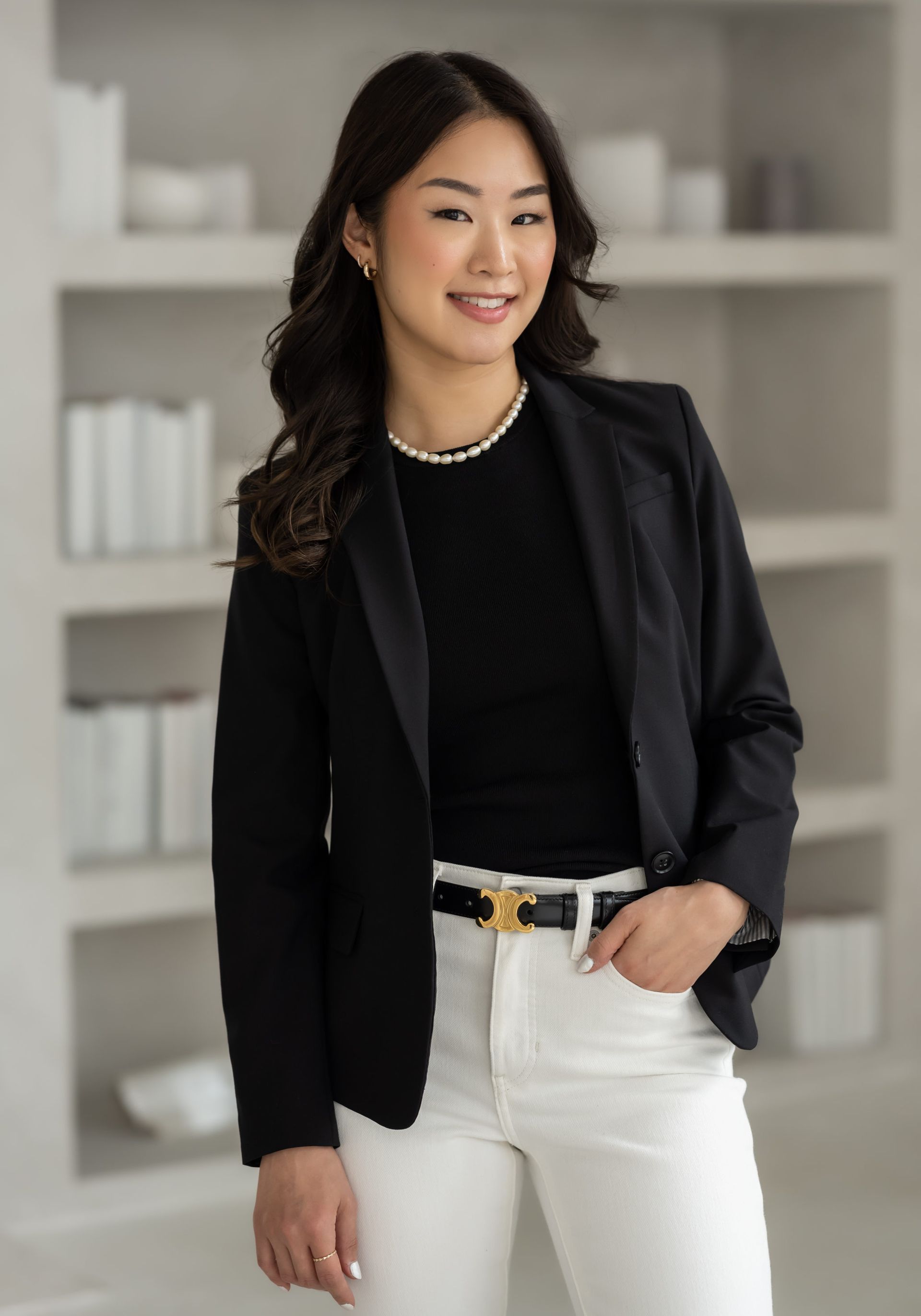 A woman wearing a black blazer and white pants poses for professional headshots.
