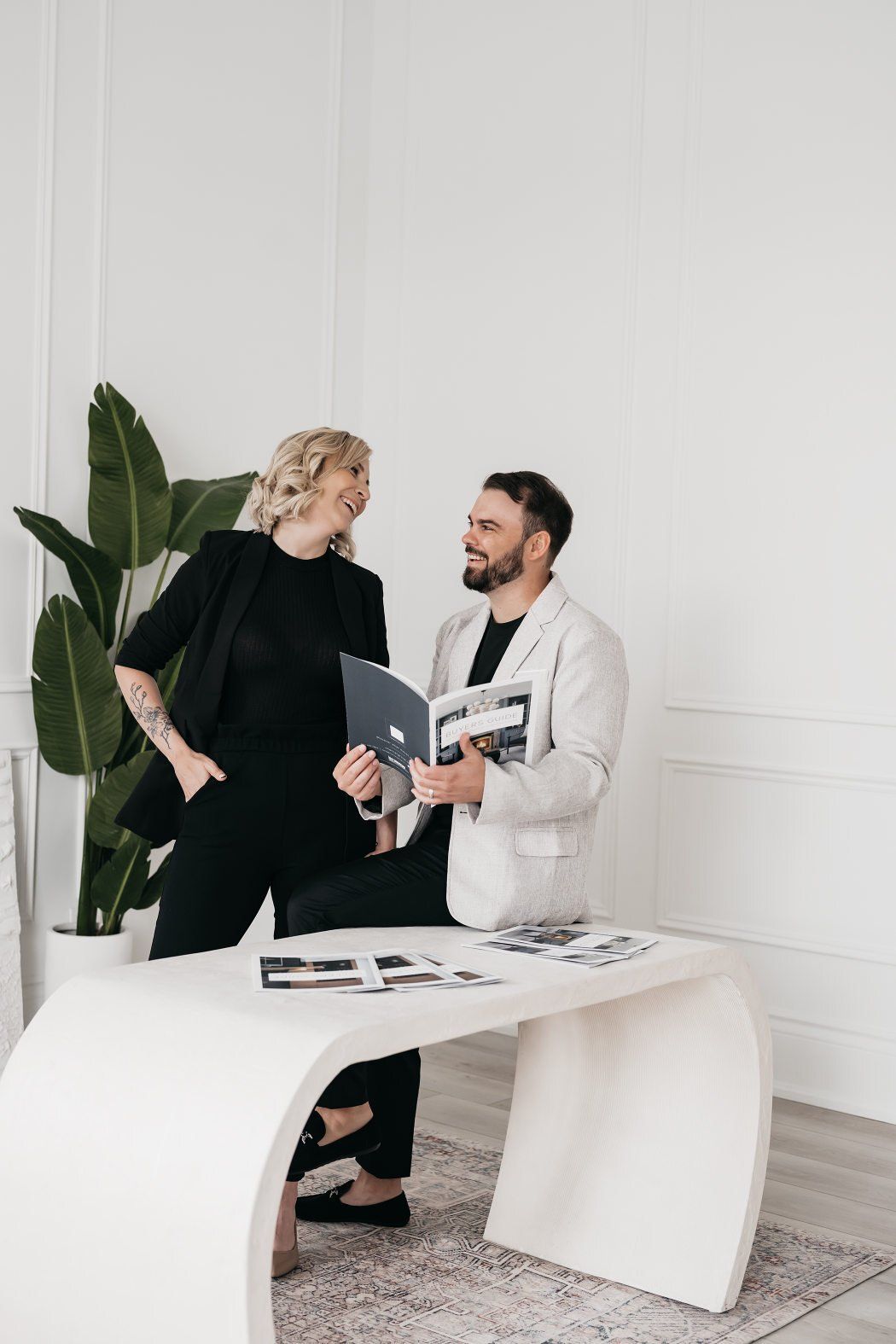 A man and woman stand side by side at a desk, looking towards each other as they converse.