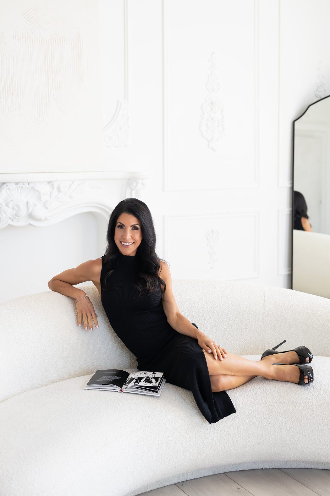 a woman wearing a black dress sitting on a white sofa
