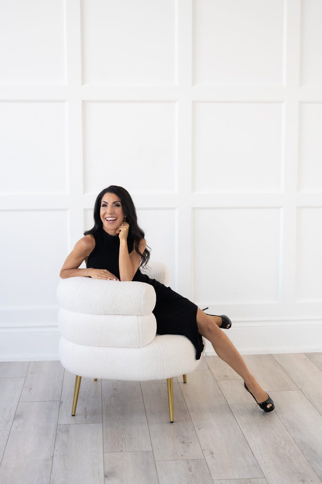 a woman wearing a black dress sitting on a white accent chair