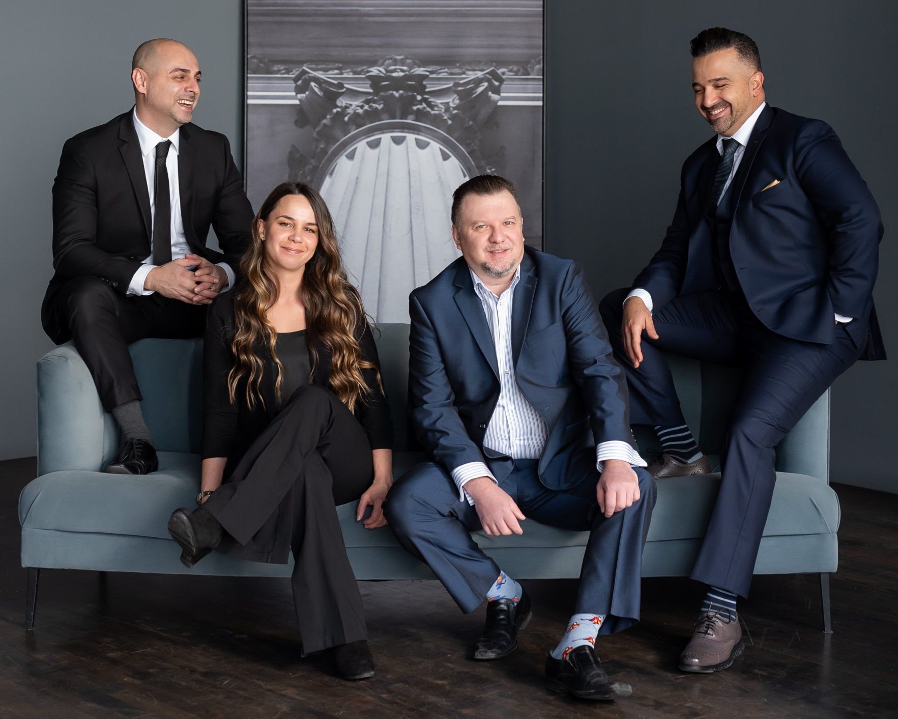 Four smartly  dressed realtors smiling and sitting on a couch.